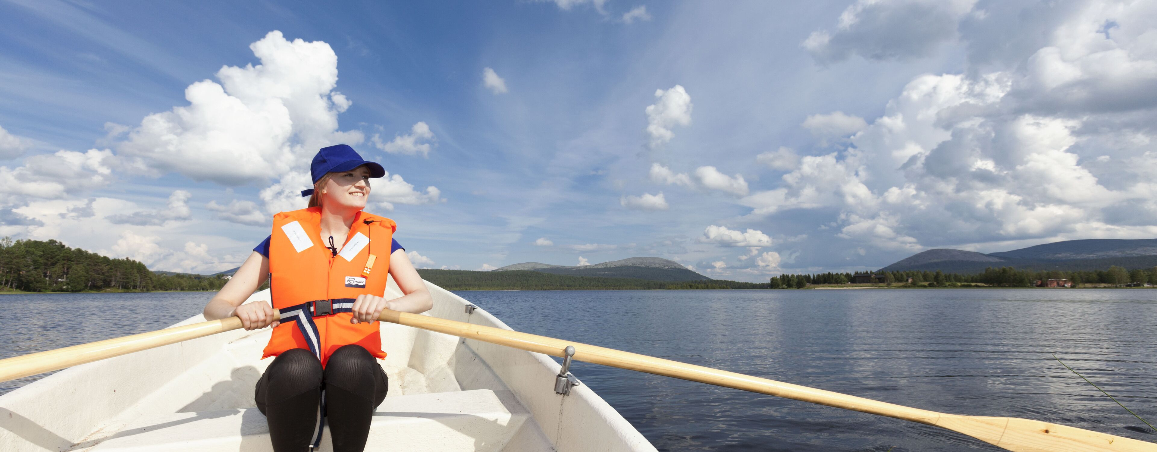 Eine Person in einem Boot, gekleidet mit einer orangefarbenen Schwimmweste und mit einem Paddel in der Hand.