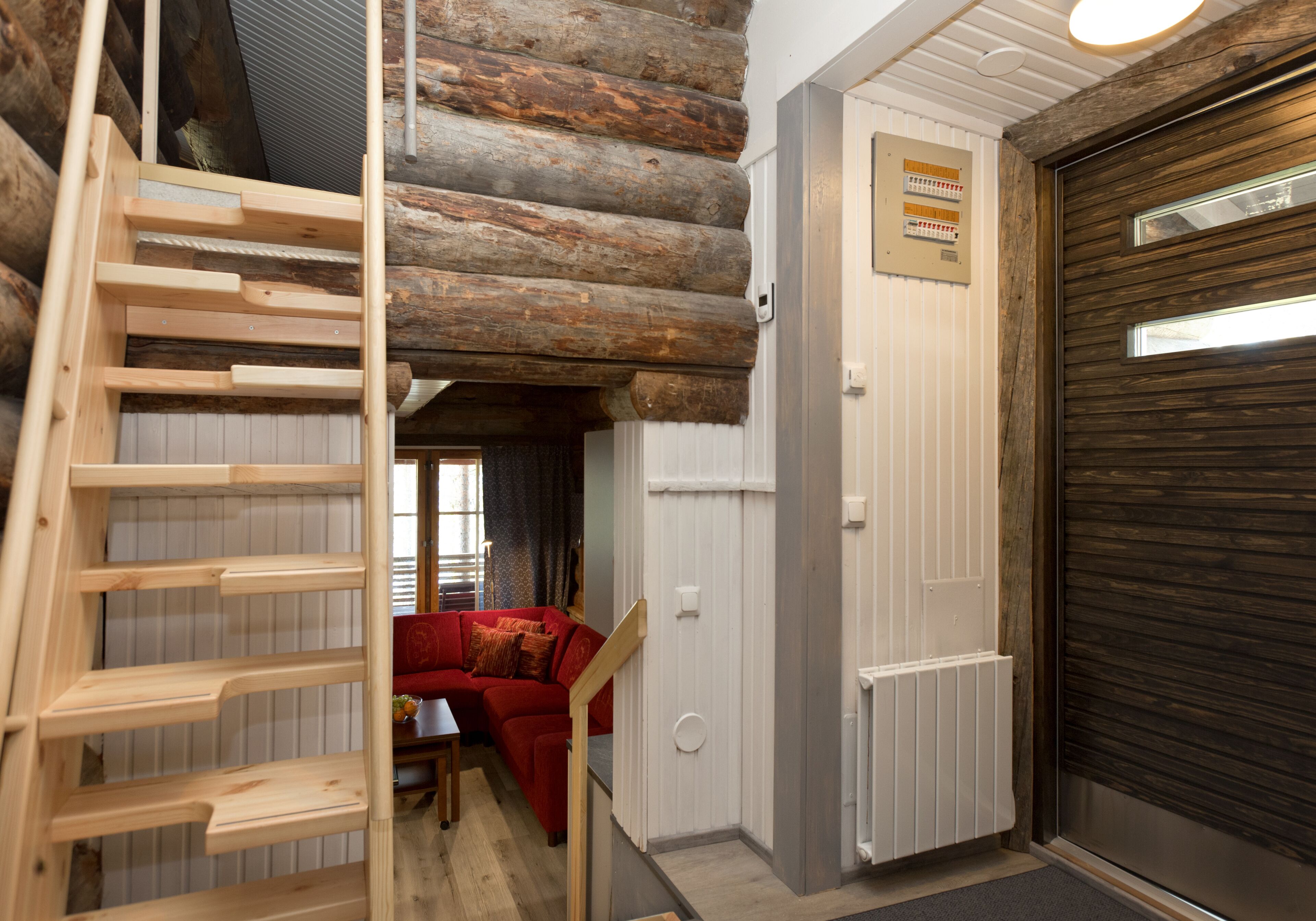 A log cabin interior with a wooden ladder, a red sofa, and a closed garage door.