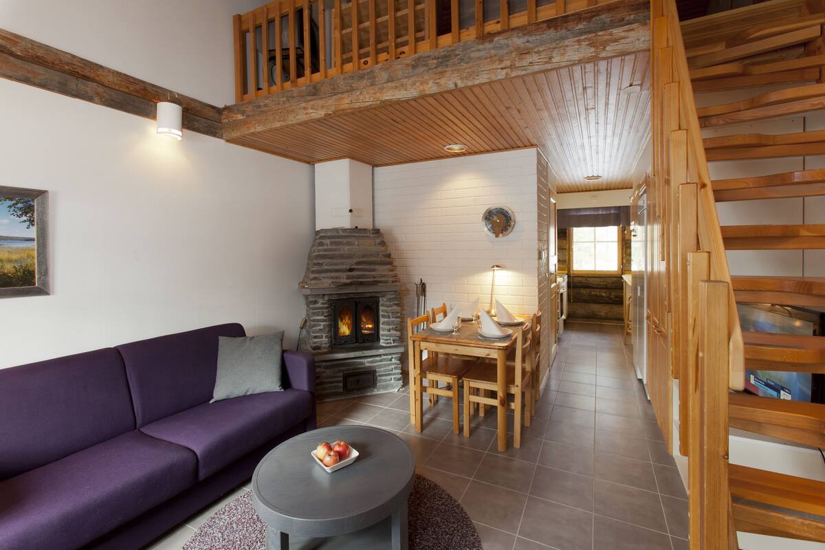 A cozy living room with a stone fireplace, wooden staircase, and a purple sofa.
