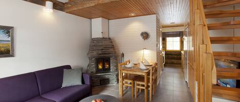 A cozy living room with a stone fireplace, wooden staircase, and a purple sofa.