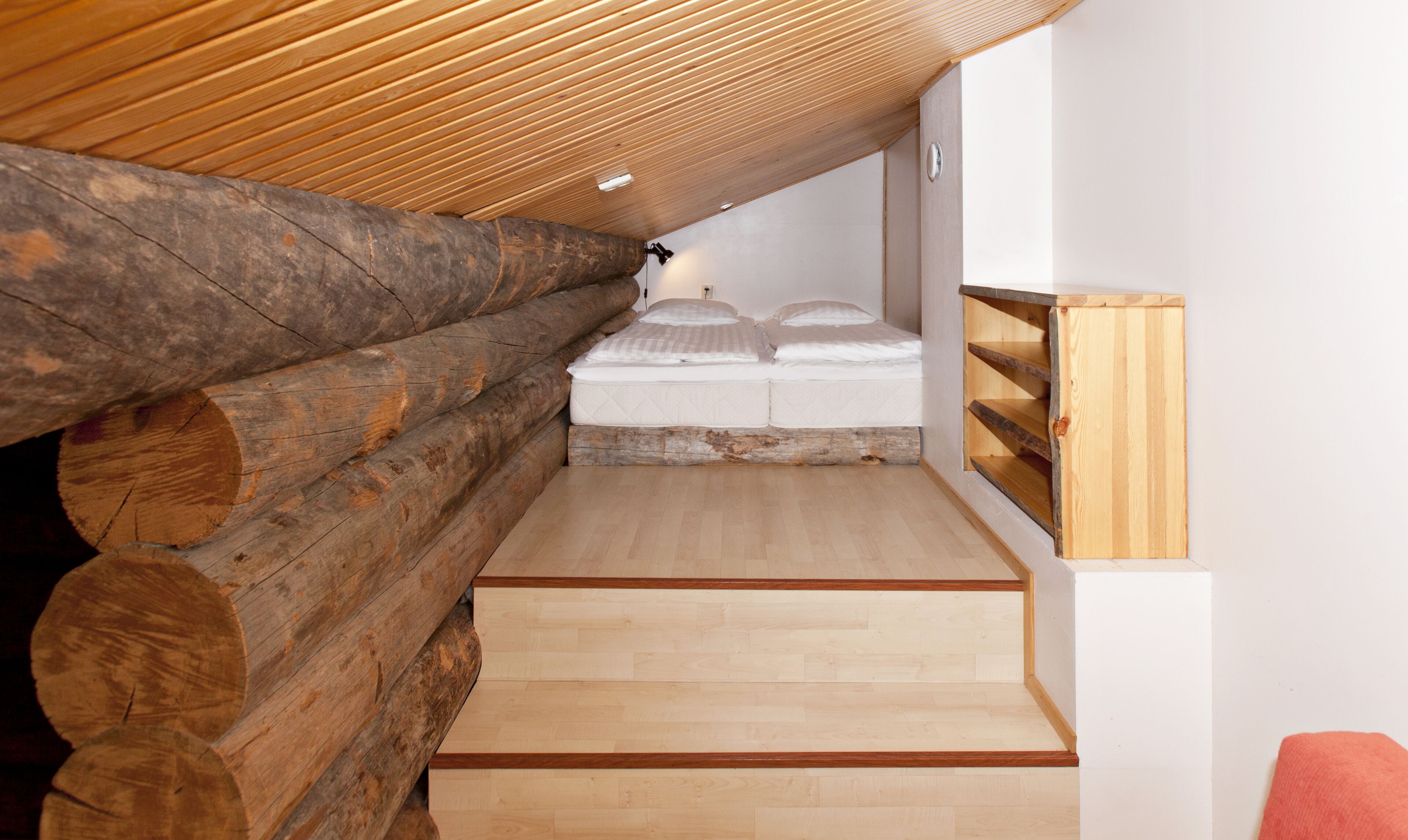 A loft bedroom with a wooden ceiling, a bed with white bedding, and a wooden bench.