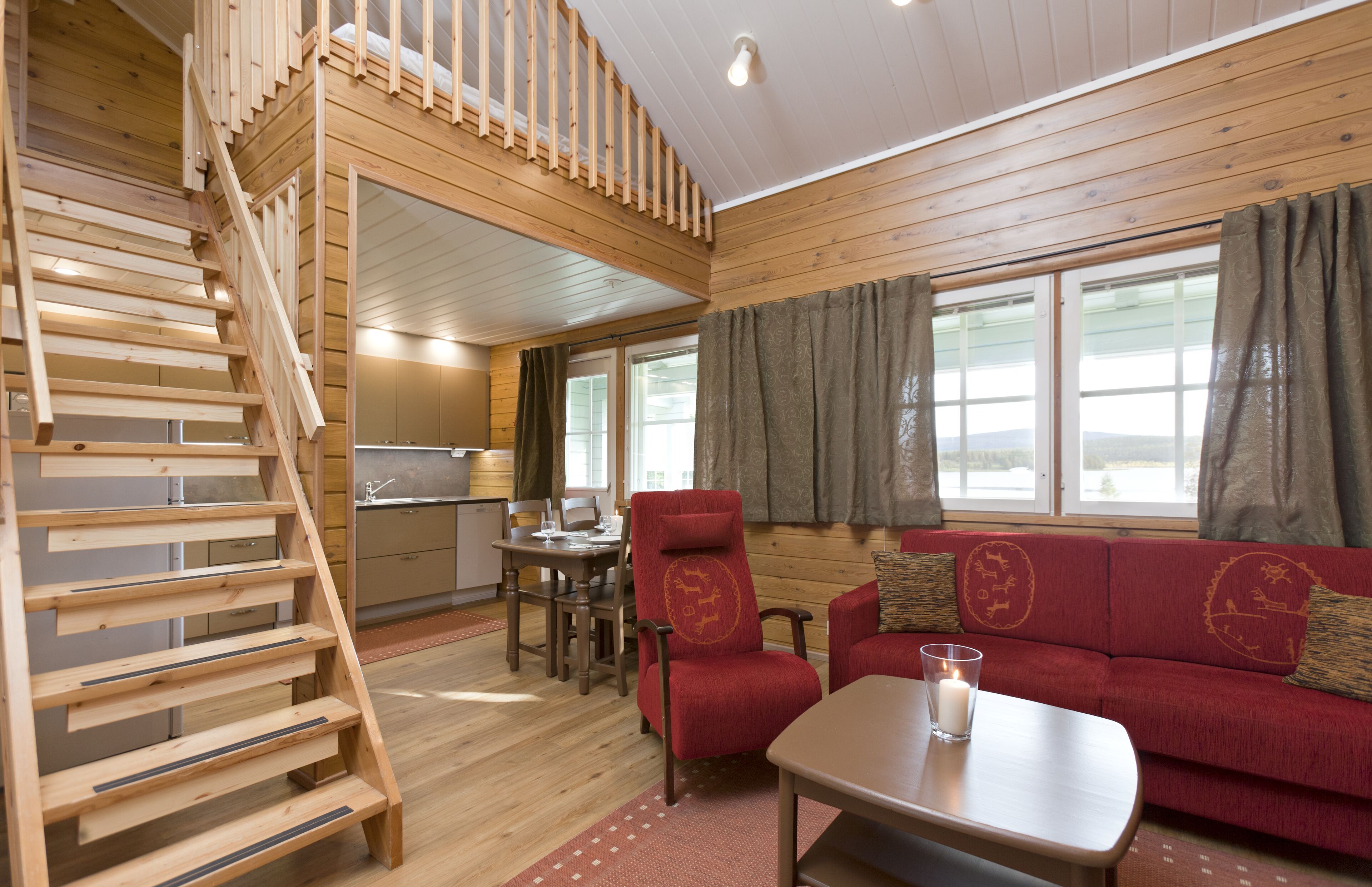 A wooden interior with a staircase, a red sofa, a dining table, and a kitchen area.