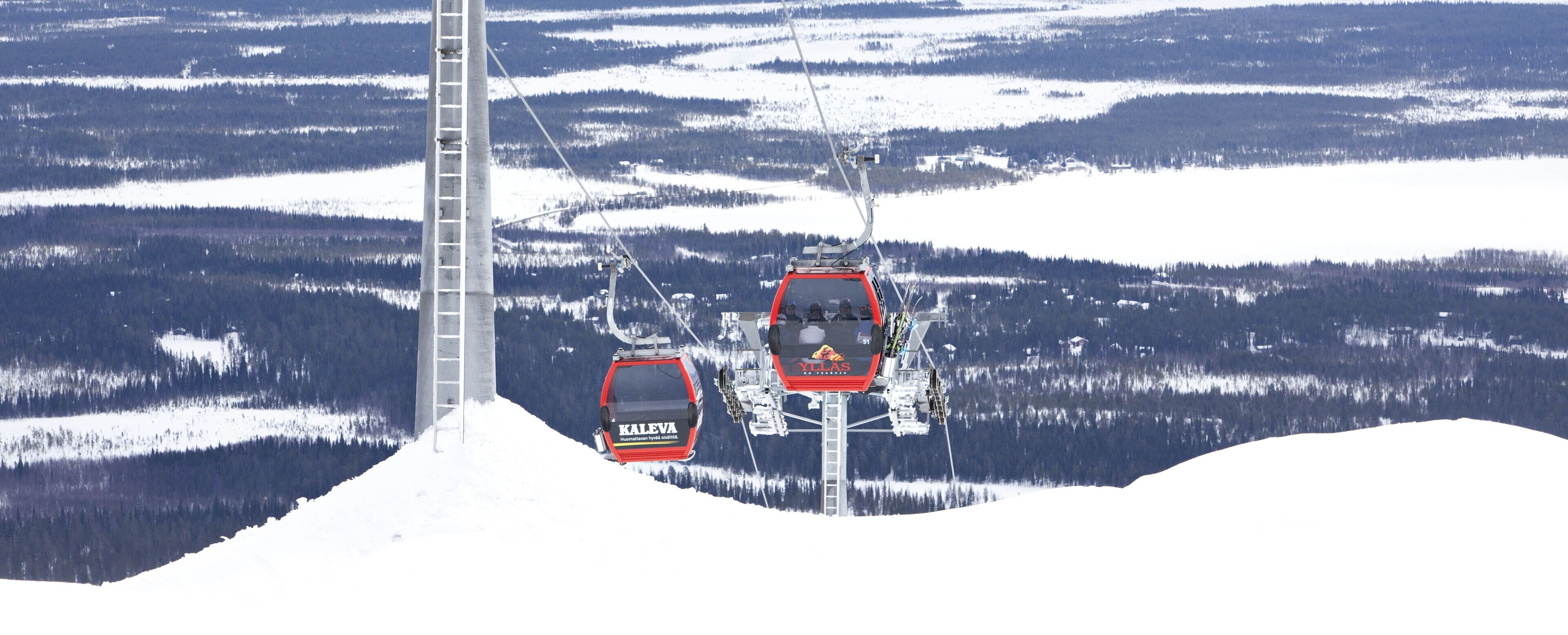 A ski lift with two cabins, one red and one black, against a snowy mountainous backdrop.