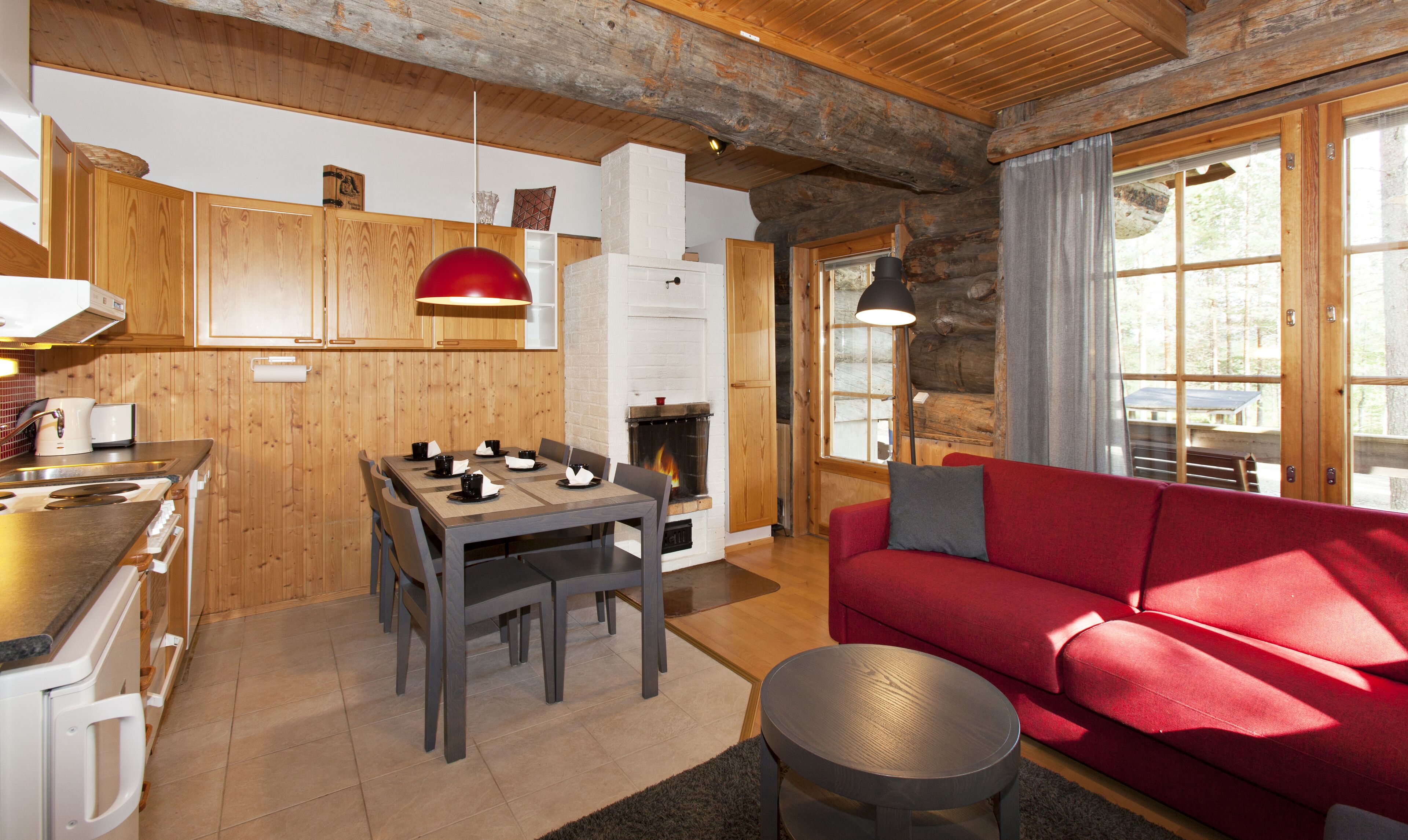 Un interior de cabaña acogedor con comedor, un sofá rojo y una chimenea.