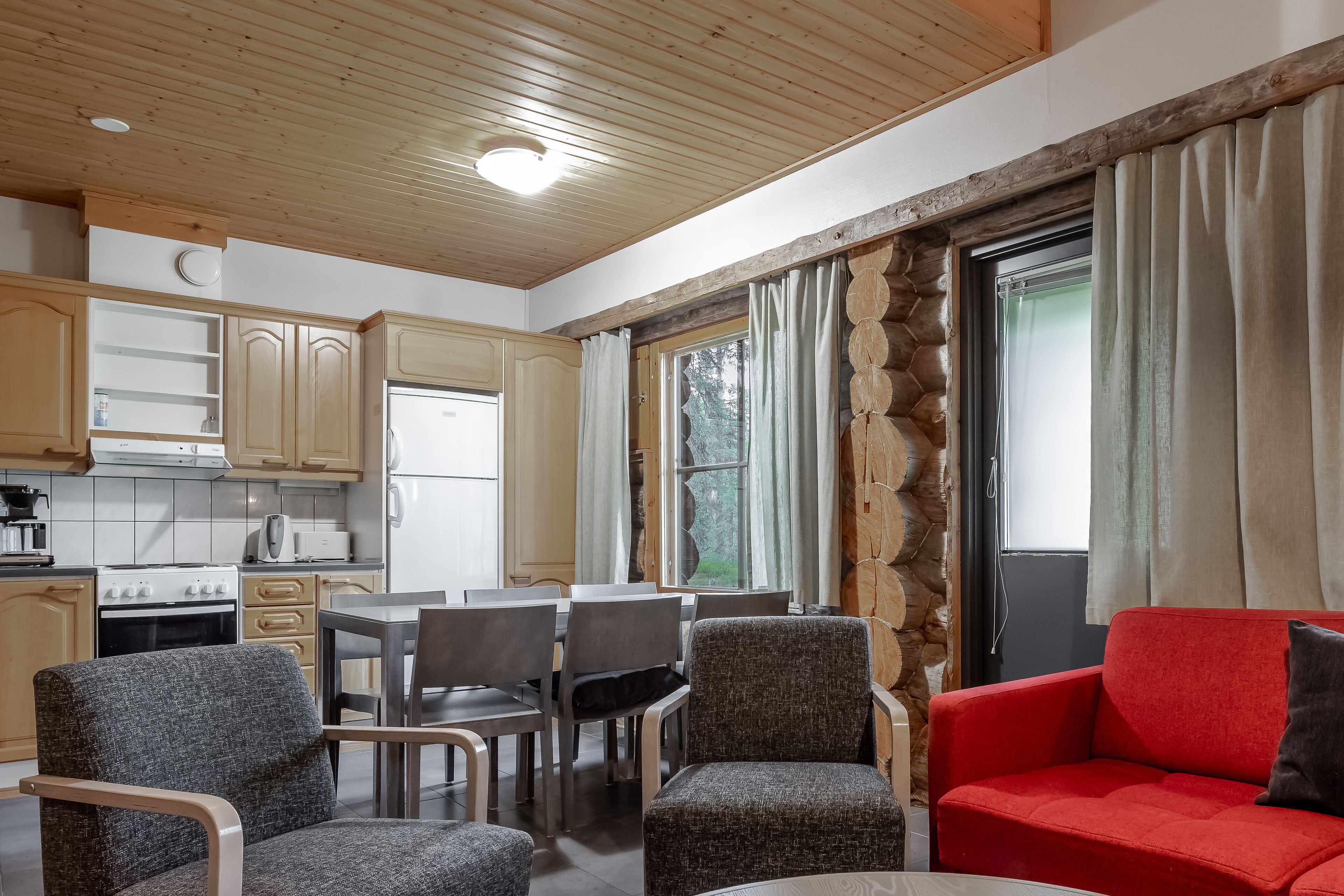Een moderne keuken met houten kastjes, een eethoek met grijze stoelen en een rode bank.
