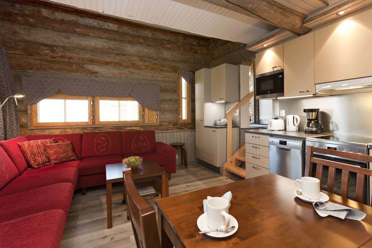 A cozy living area with a red sofa, wooden dining table, and a kitchen with modern appliances.