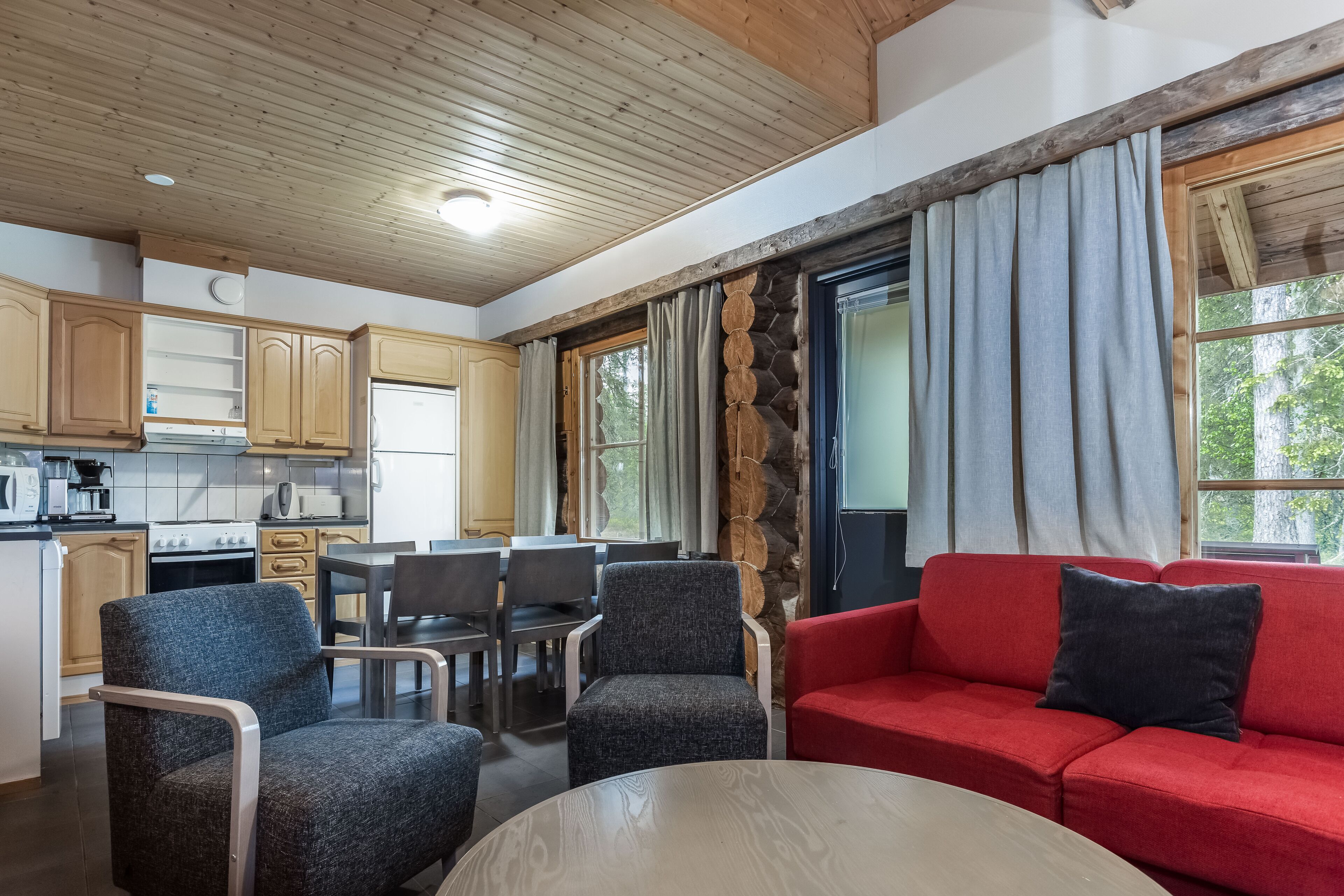 Una cuina moderna amb armaris de fusta, una zona de menjador amb cadires, un sofà vermell i una finestra gran amb cortines.