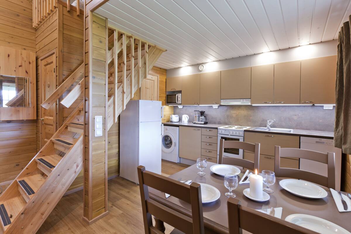 A modern kitchen with wooden cabinetry, a built-in oven, and a dining area with a table set for two.
