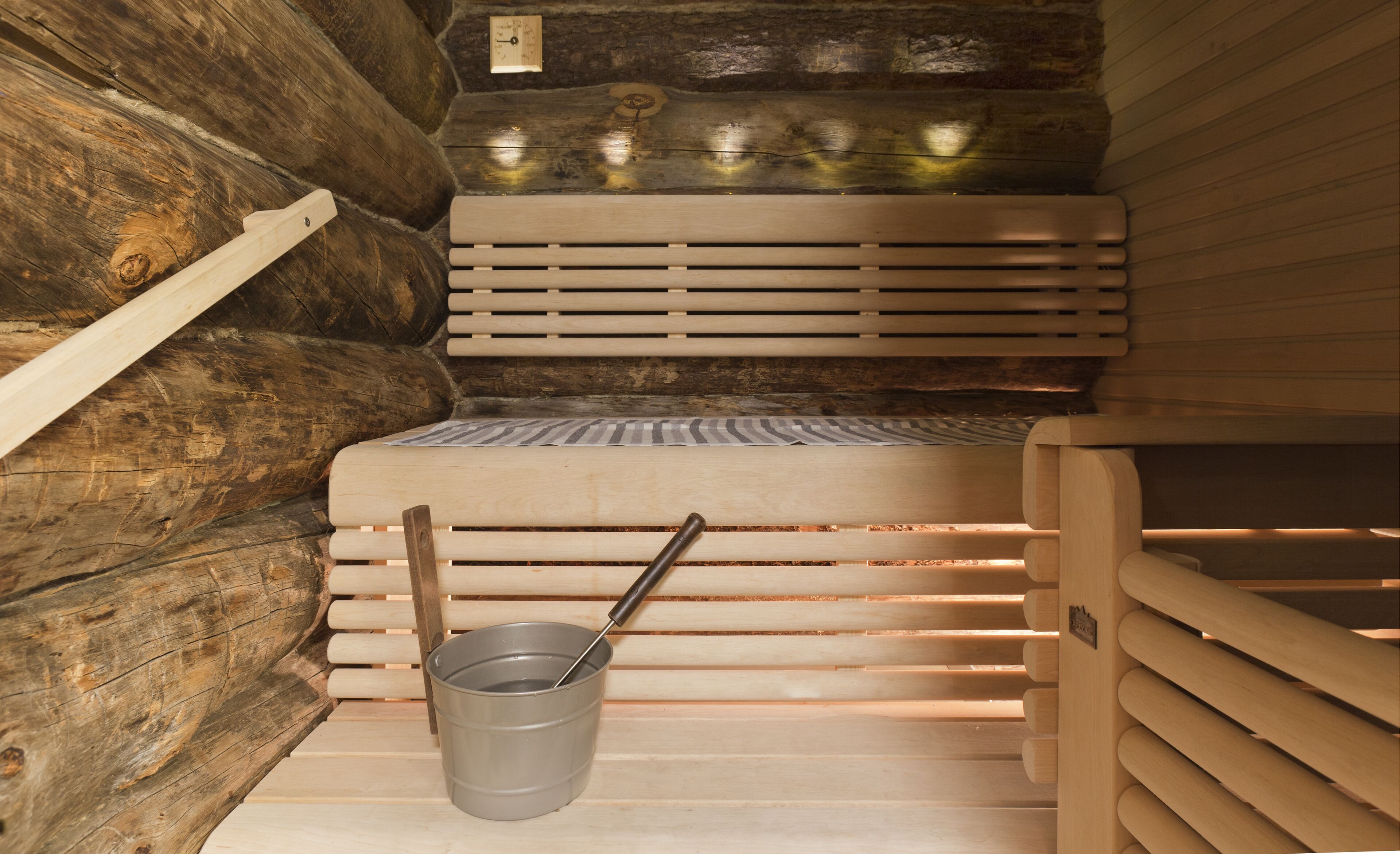 Un sauna avec des bancs en bois et un seau en métal.