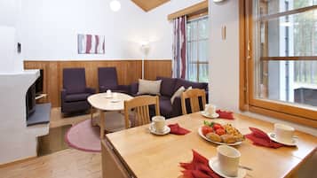 Une pièce chaleureuse avec une table à manger en bois, mise pour le petit-déjeuner, un canapé et une cheminée.