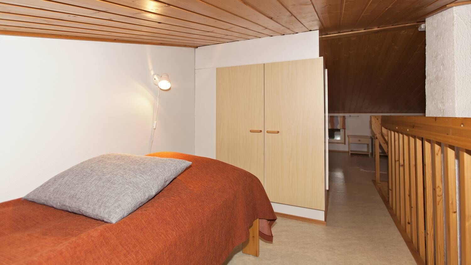 Quarto com uma cama, guarda-roupa e um corrimão de madeira.