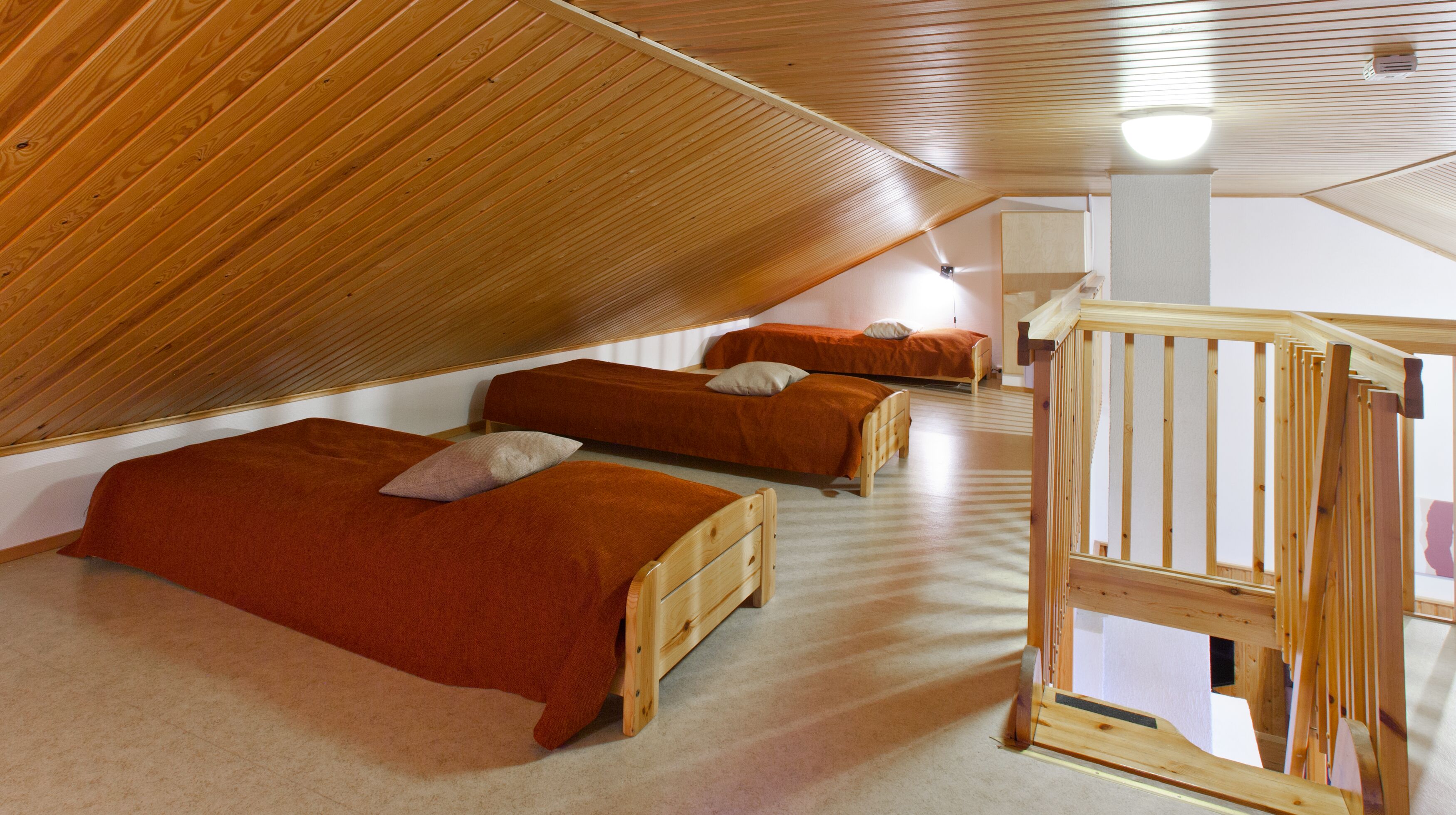 Una habitación con dos camas de madera, una escalera de madera y techo inclinado.