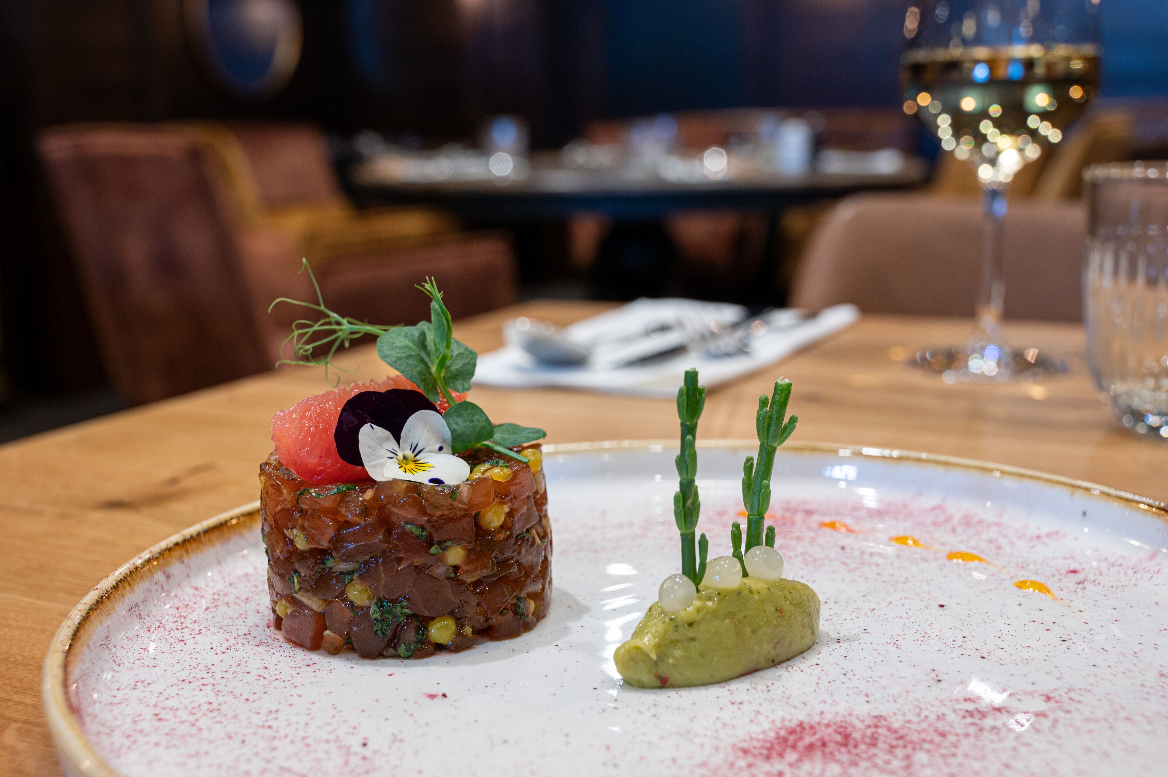 Une assiette avec un plat décoré et un verre de vin, posés sur une table.