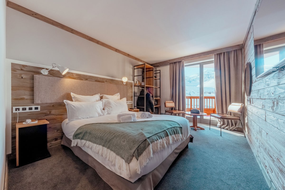 Une chambre d’hôtel avec un grand lit, une table de chevet, un bureau, une chaise, une bibliothèque et une vue sur l’extérieur.