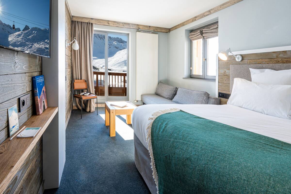 Une chambre d’hôtel avec un lit, un bureau, une chaise, une télévision et une vue sur les montagnes.