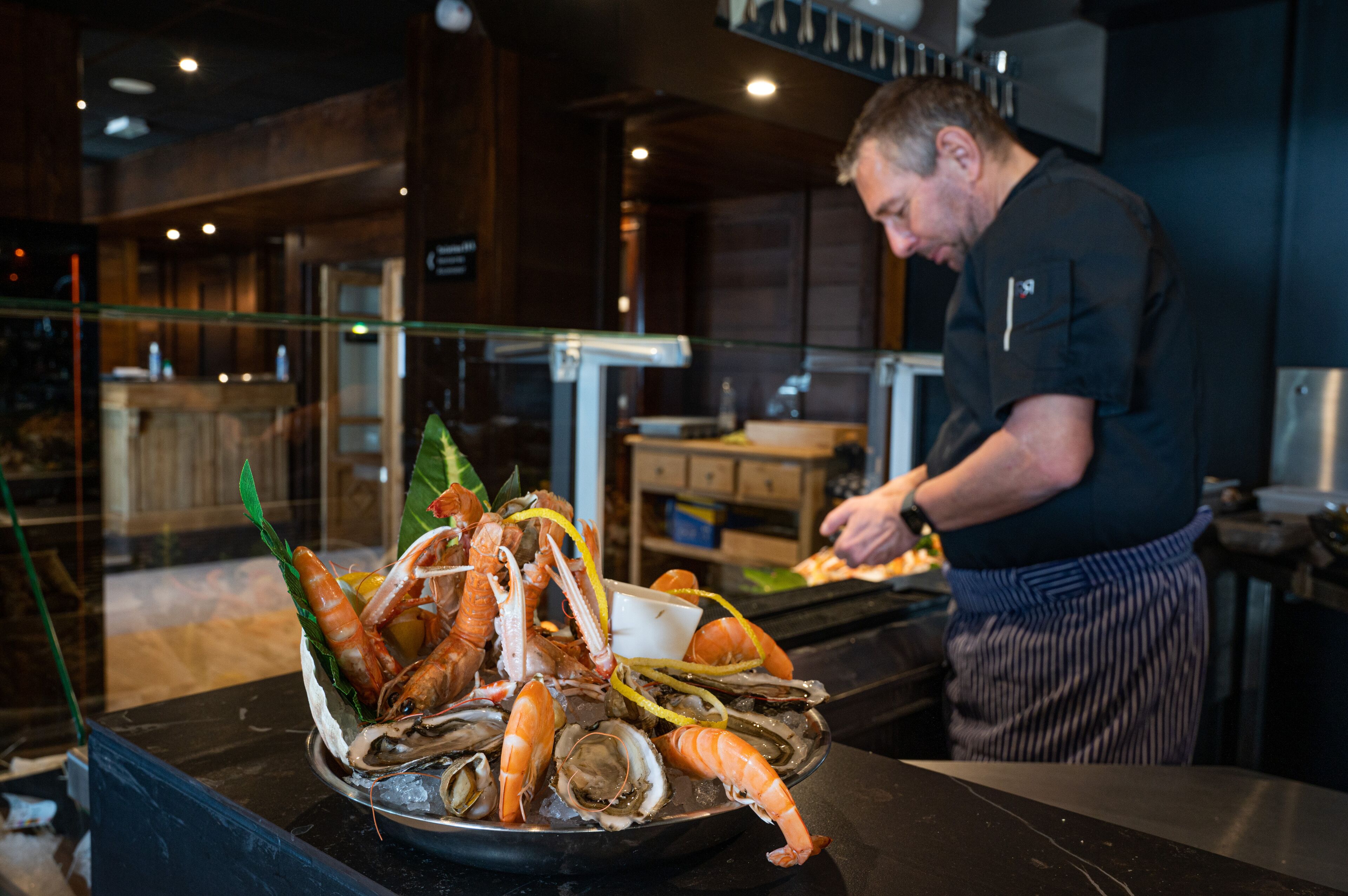 A seafood platter with various shellfish and a chef preparing food in a kitchen.