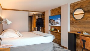 A bedroom with a bed, a desk, a chair, a mirror, and a picture on the wall. - Hôtel Le Levanna by Les Etincelles (Tignes)