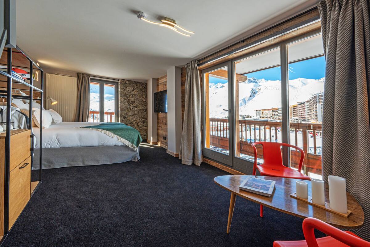 Une chambre d’hôtel avec un lit, un bureau, une chaise et une vue sur une montagne enneigée.