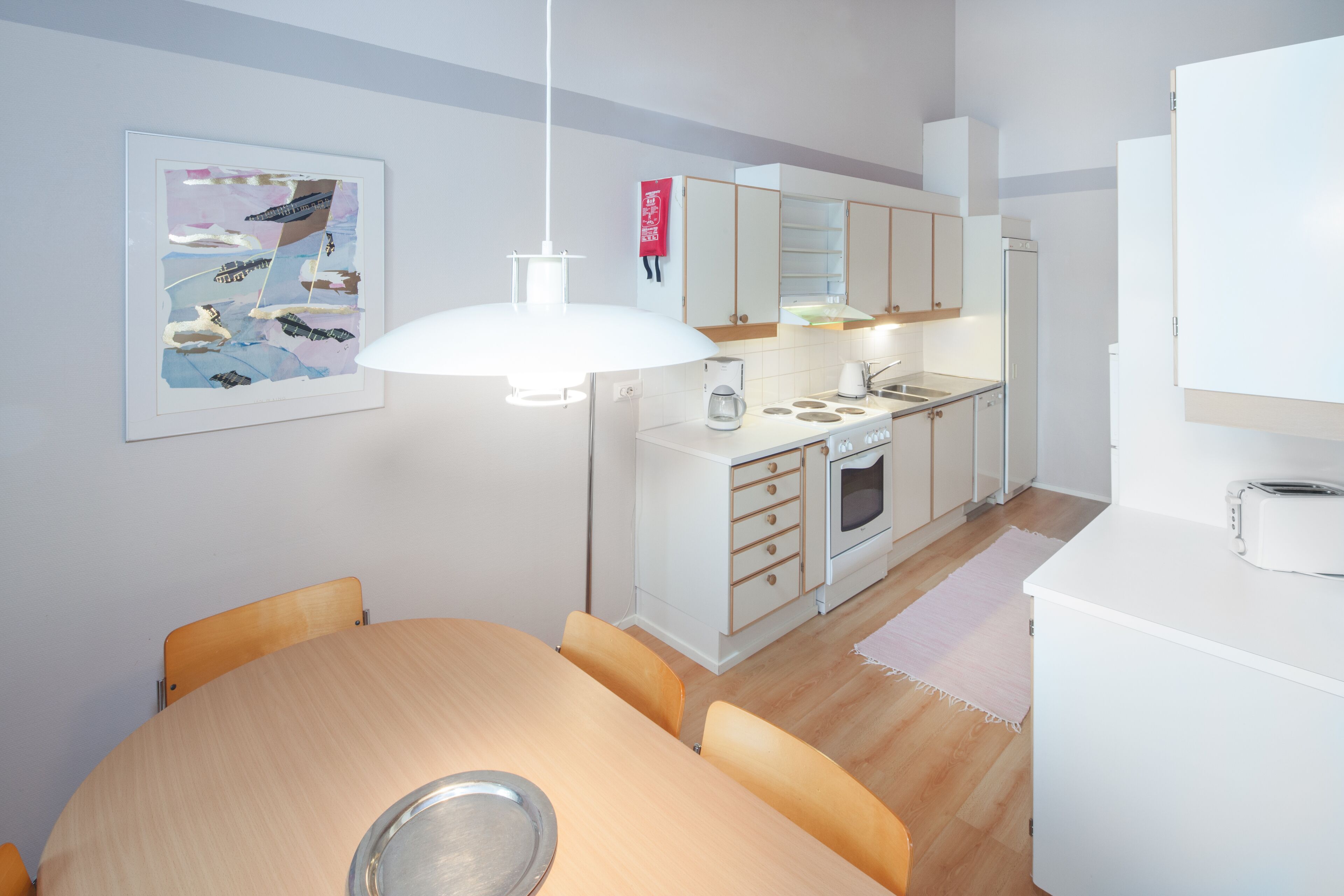 A modern kitchen with white cabinets, a dining table with chairs, and a hanging light fixture.