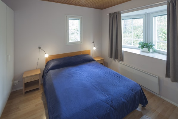 Un dormitorio con cama, mesitas de noche, una ventana con cortinas y una planta en el alféizar.
