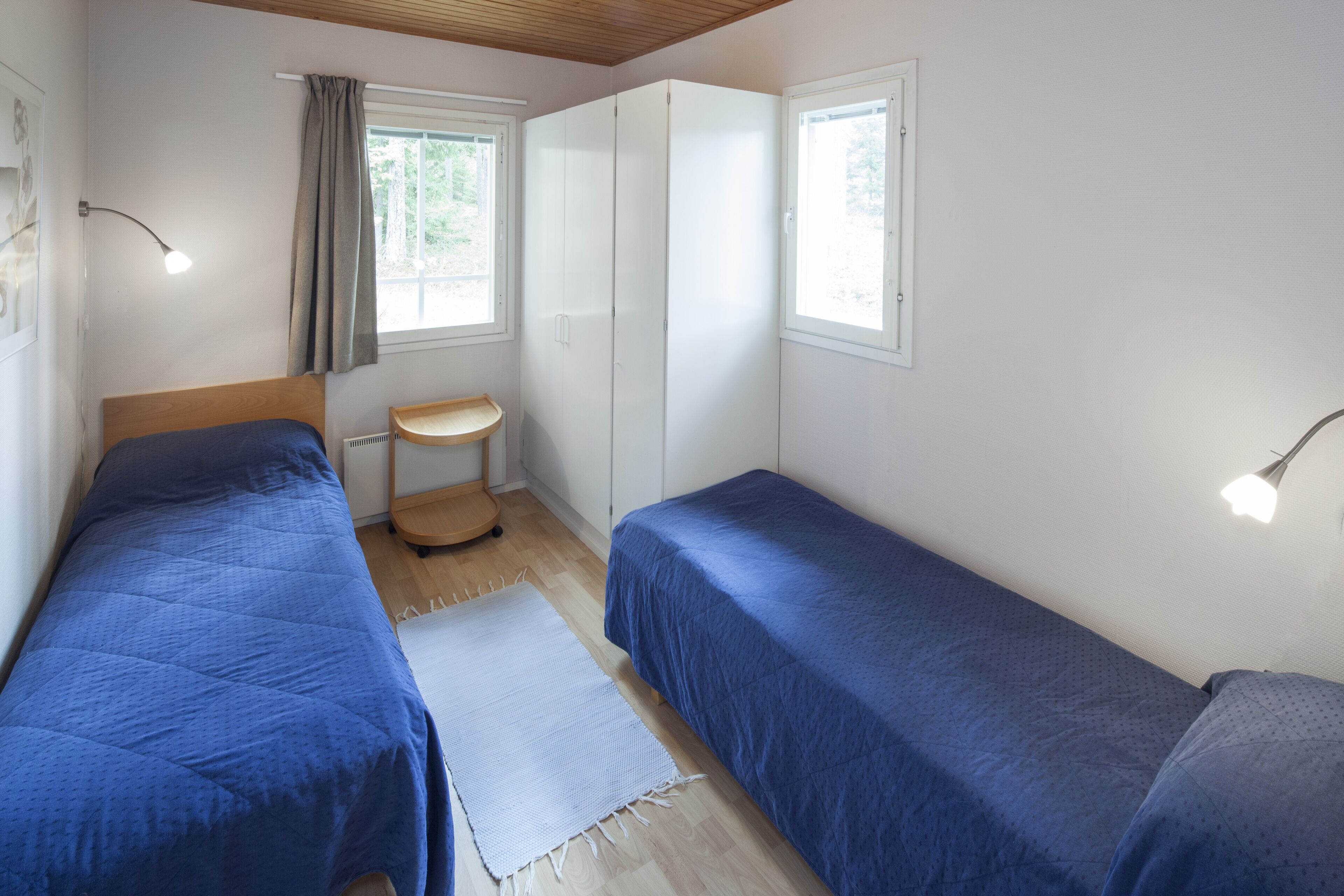 Un dormitorio con dos camas individuales, una mesita de noche pequeña, una ventana con cortinas e iluminación en el techo.