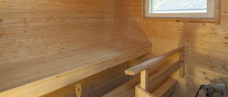 Interior de una cabaña de madera con ventana, un banco de madera, un balde y un recipiente con leña.