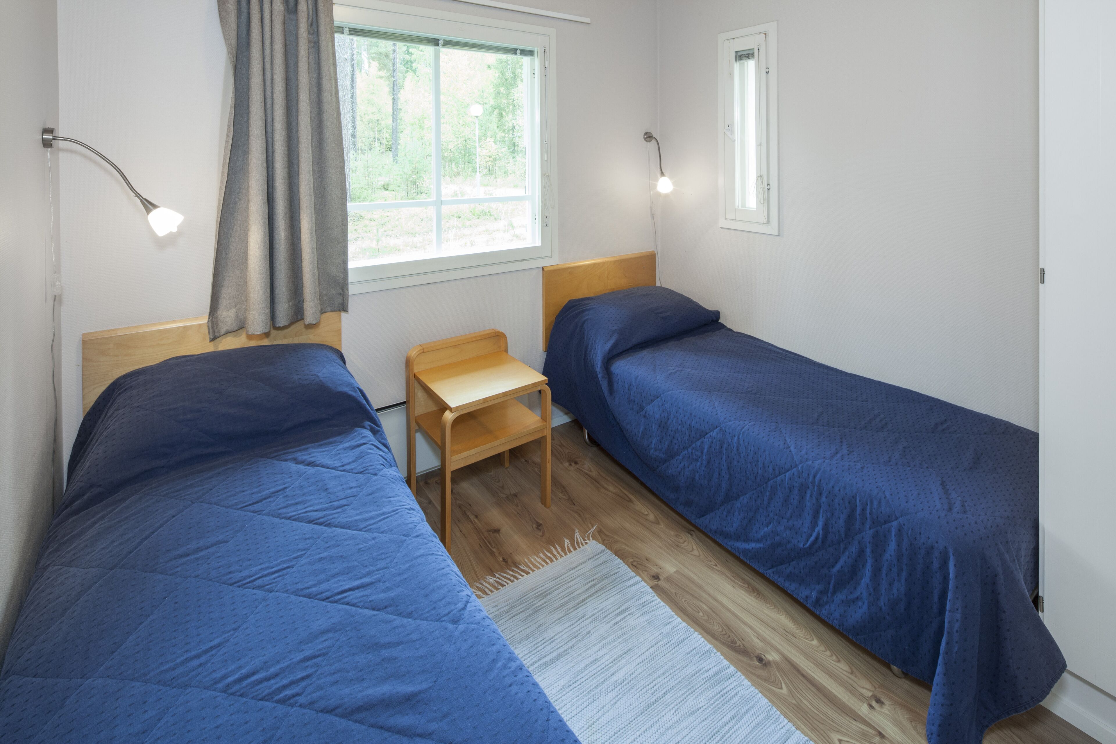 A room with two beds, a small wooden table, and a window with curtains.