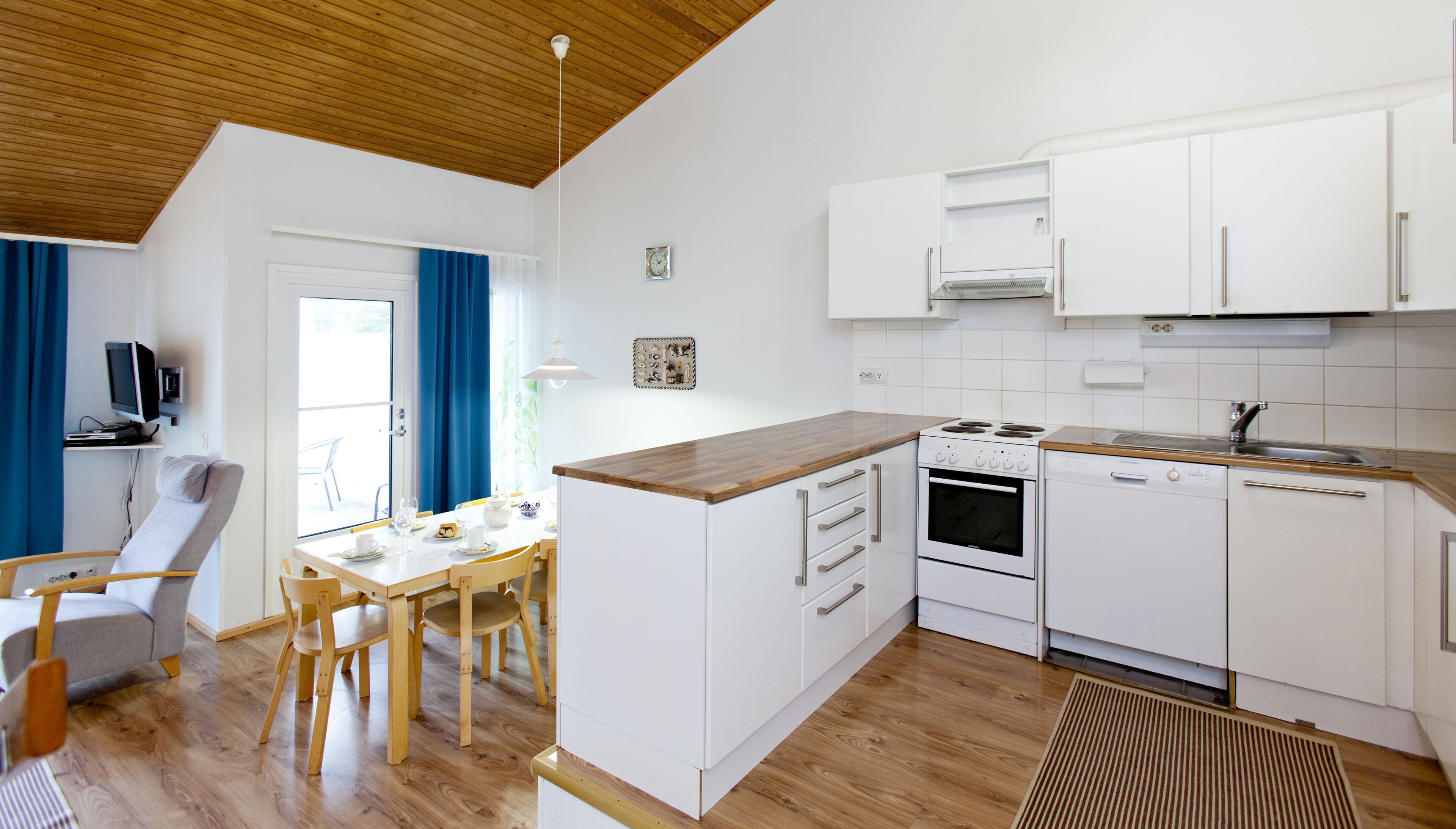 A modern kitchen with white cabinets, a wooden countertop, and a dining area with a table and chairs.