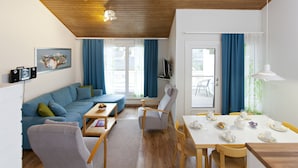 A modern living room with a sofa, coffee table, and dining table set for a meal. - Holiday Club Airisto (Pargas)