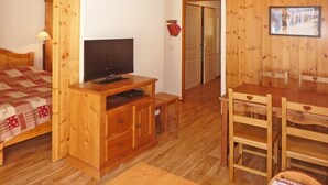 A wooden room with a bed, a TV on a wooden stand, a dining table with chairs, and a door leading to another room. - Les Orres 1800: apt for 6, heated pool, sauna, ski-in/ski-out (Les Orres)