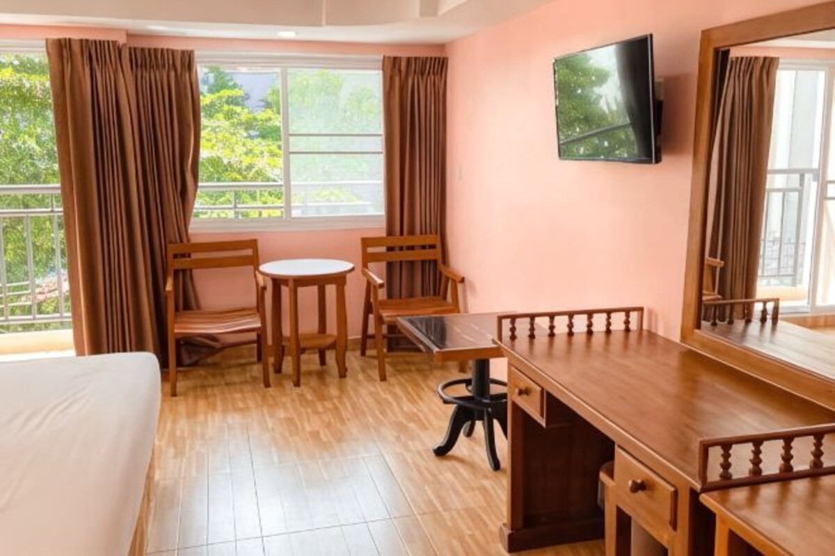 Une pièce comprenant un lit, un bureau, deux chaises, un téléviseur et une fenêtre avec des rideaux.