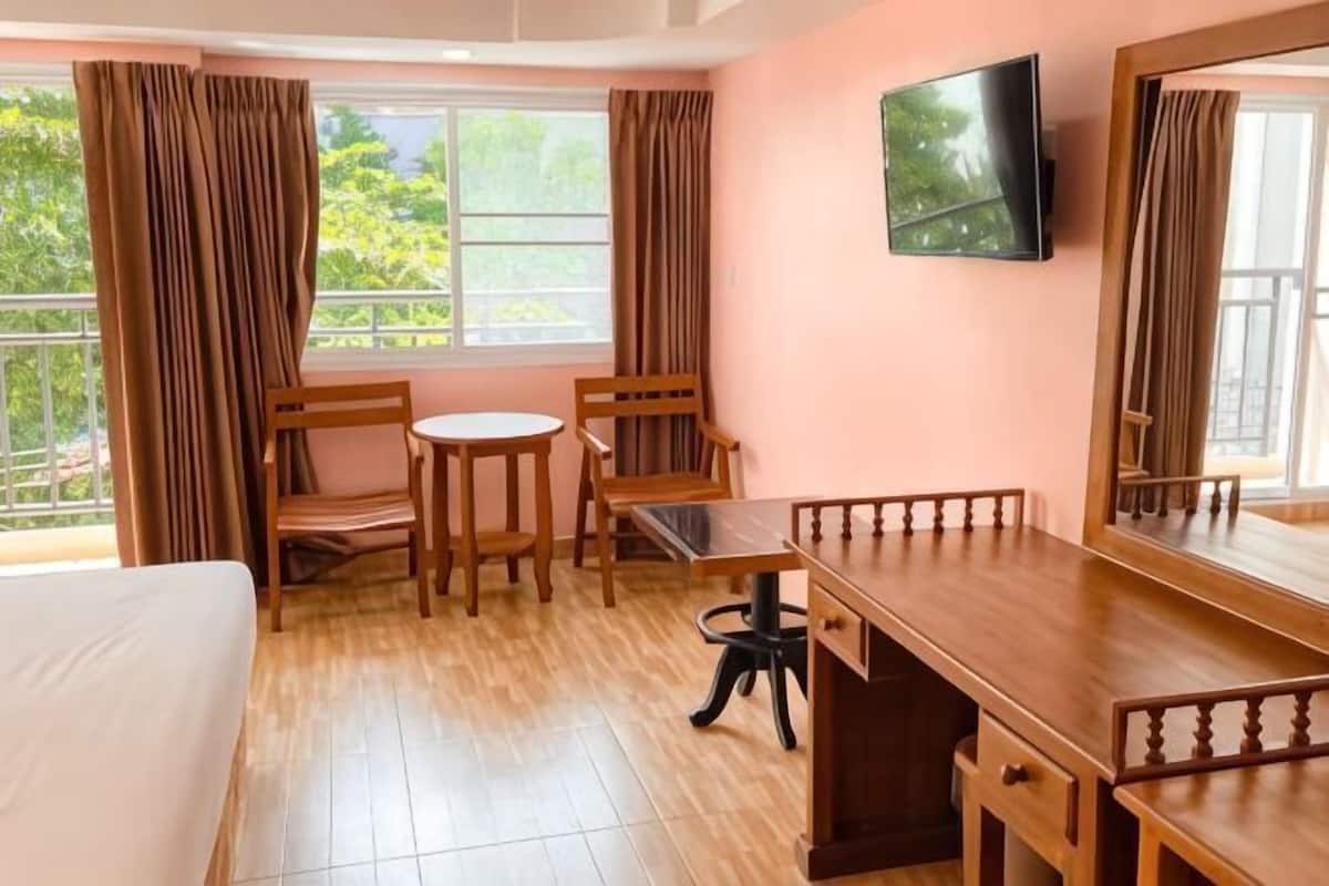Een kamer met een bed, een bureau, twee stoelen, een televisie en een raam met gordijnen.
