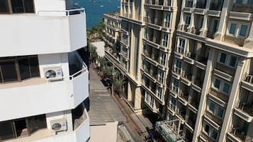 Un edificio de varios pisos con balcones, vista al mar y una calle con vehículos y peatones.