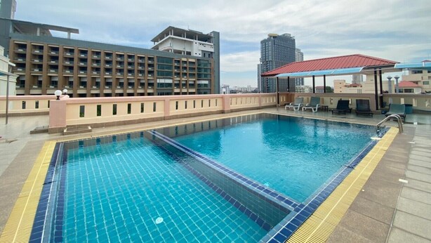 A rooftop swimming pool with a tiled deck, a covered seating area, and modern buildings in the background. - A.A. Pattaya Golden Beach Hotel (Pattaya)