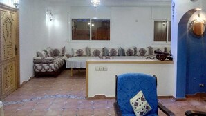Una habitación con un conjunto de sofás, un sillón azul, una mesita y un adorno en la pared.