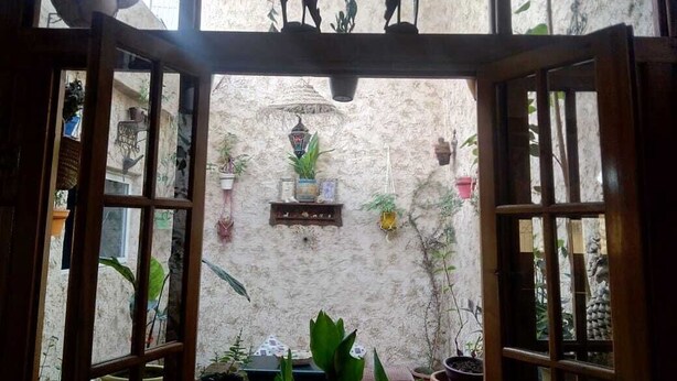Una puerta de madera abierta que da a un patio con plantas en macetas y un farol colgante.