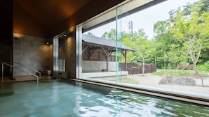A modern indoor swimming pool with clear glass walls, a wooden deck outside, and a view of a green landscape. - Urabandai Lakeresort Nekomarikyu (Kitashiobara)
