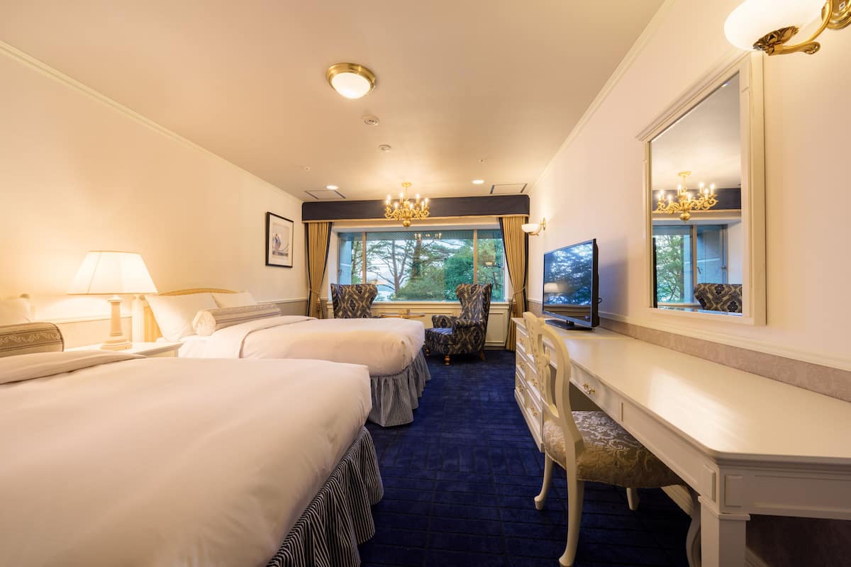 A hotel room with two beds, a desk, a chair, a television, and a large mirror.