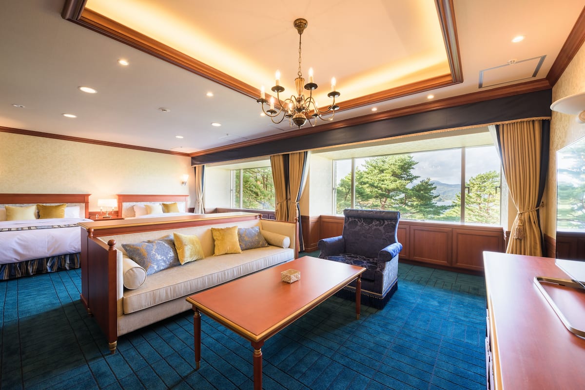 A hotel room with a bed, sofa, armchair, and a dining table.