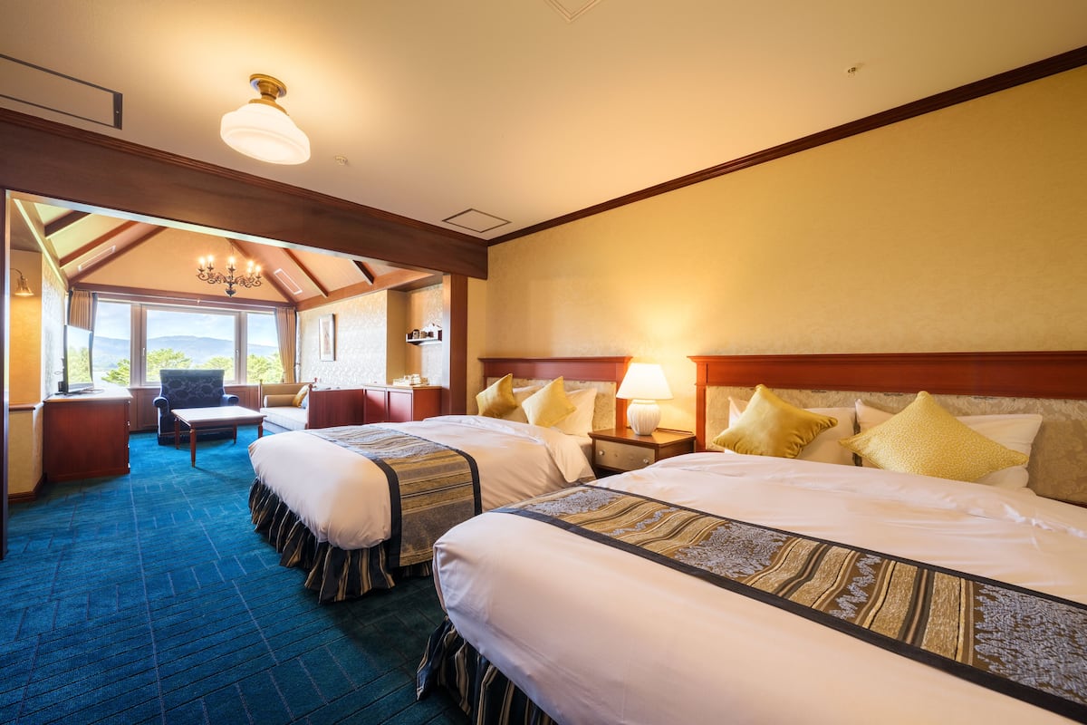 A hotel room with two beds, a sofa, a desk, and a chandelier.