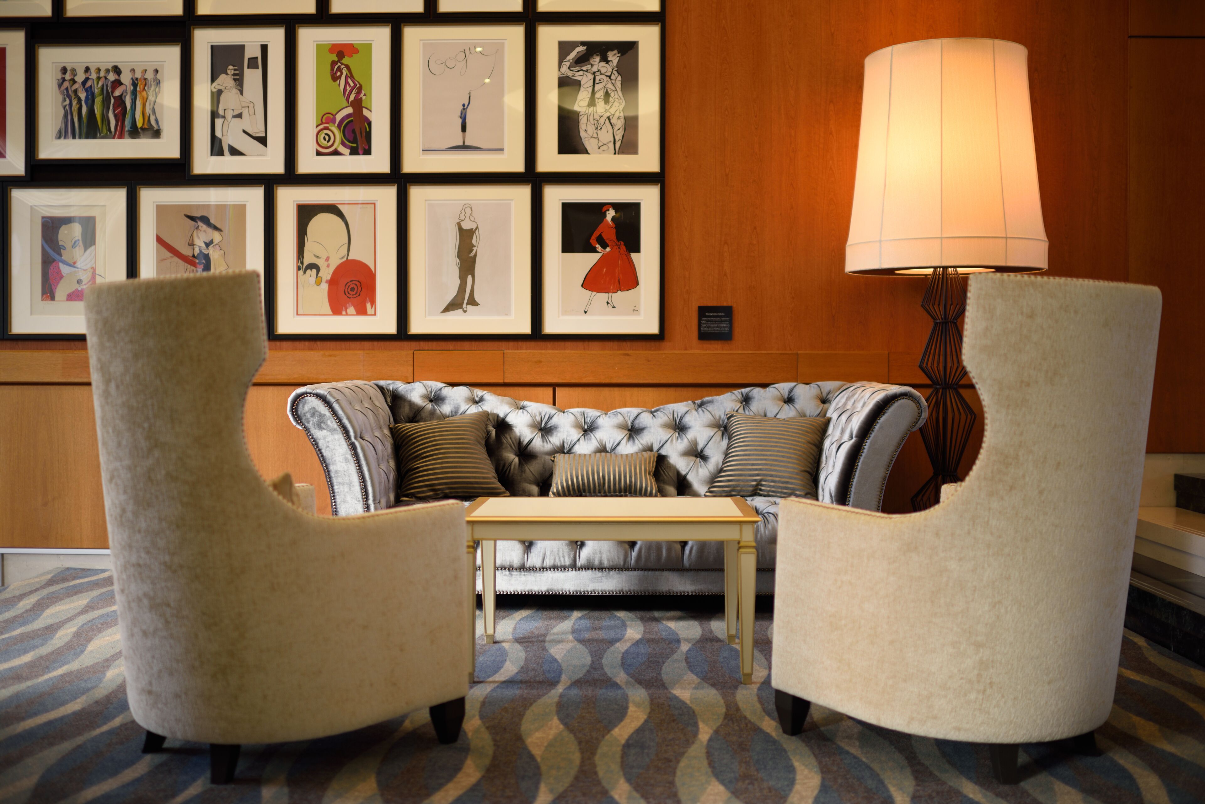 A room with a tufted sofa, two armchairs, a small table, and a wall adorned with framed artwork.