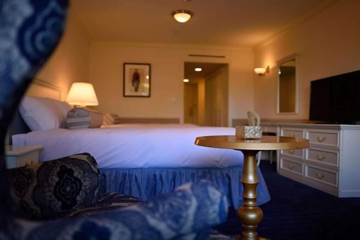 A hotel room with a bed, bedside table, lamp, dresser, and a television.