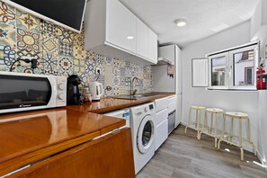 A compact kitchen with a washing machine, a coffee maker, and a microwave. - Bica Ropers Suite, Studio apartment in the heart of the city (Lisbon)