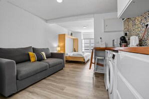 A modern, compact living space with a grey sofa, a wooden desk, a bed, and a washing machine. - Bica Ropers Suite, Studio apartment in the heart of the city (Lisbon)