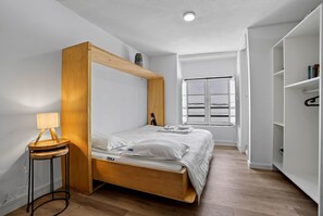 A bedroom with a wooden four-poster bed, a bedside table with a lamp, a window with blinds, and a wardrobe. - Bica Ropers Suite, Studio apartment in the heart of the city (Lisbon)