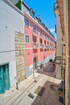 A narrow street with a pink building featuring balconies and a stone wall on one side. - Bica Ropers Suite, Studio apartment in the heart of the city (Lisbon)