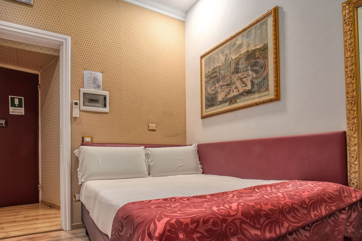 A hotel room with a bed, a painting on the wall, and a wooden floor.