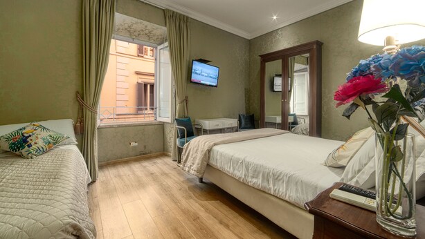 A hotel room with two beds, a desk, a TV, and a vase with flowers. - Bq House Trevi Luxury Rooms (Rome)
