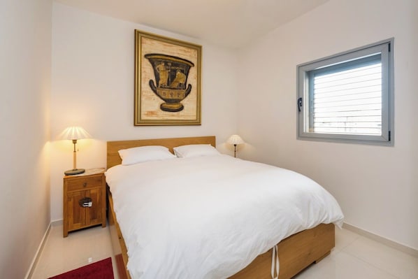 Une chambre à coucher avec un lit, deux tables de chevet avec des lampes, une fenêtre et un tableau encadré au mur.