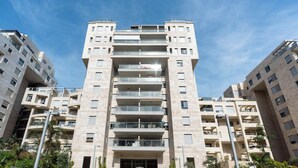 Un immeuble résidentiel à plusieurs étages, doté de balcons, d’une entrée principale et entouré de verdure.